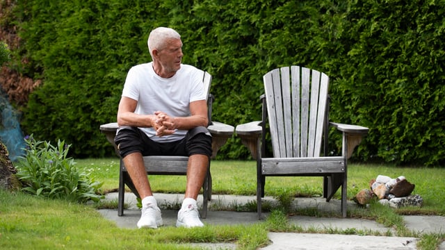 En mannlig pårørende til uhelbredelig brystkreft sitter alene ute i hagen. Foto.