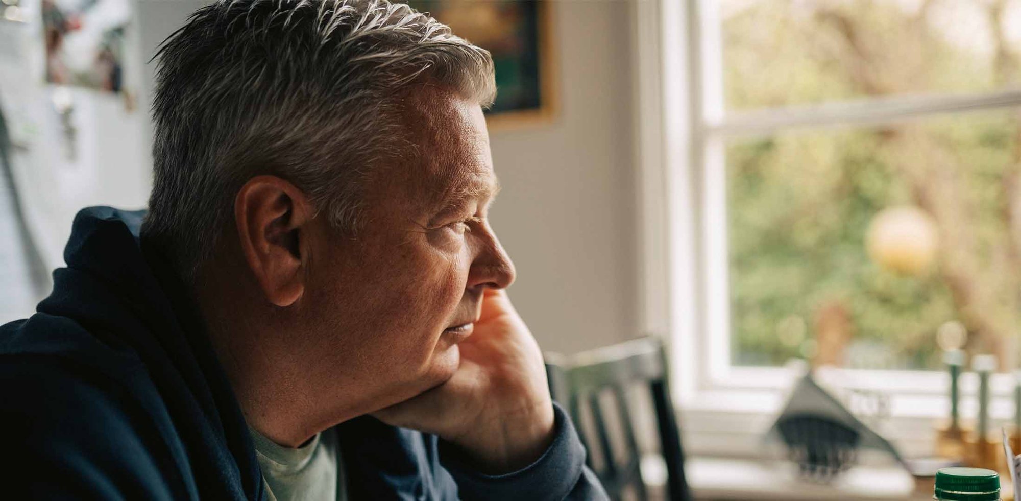 Pårørende mann til kreftsyk samboer sitter tankefull på kjøkkenet