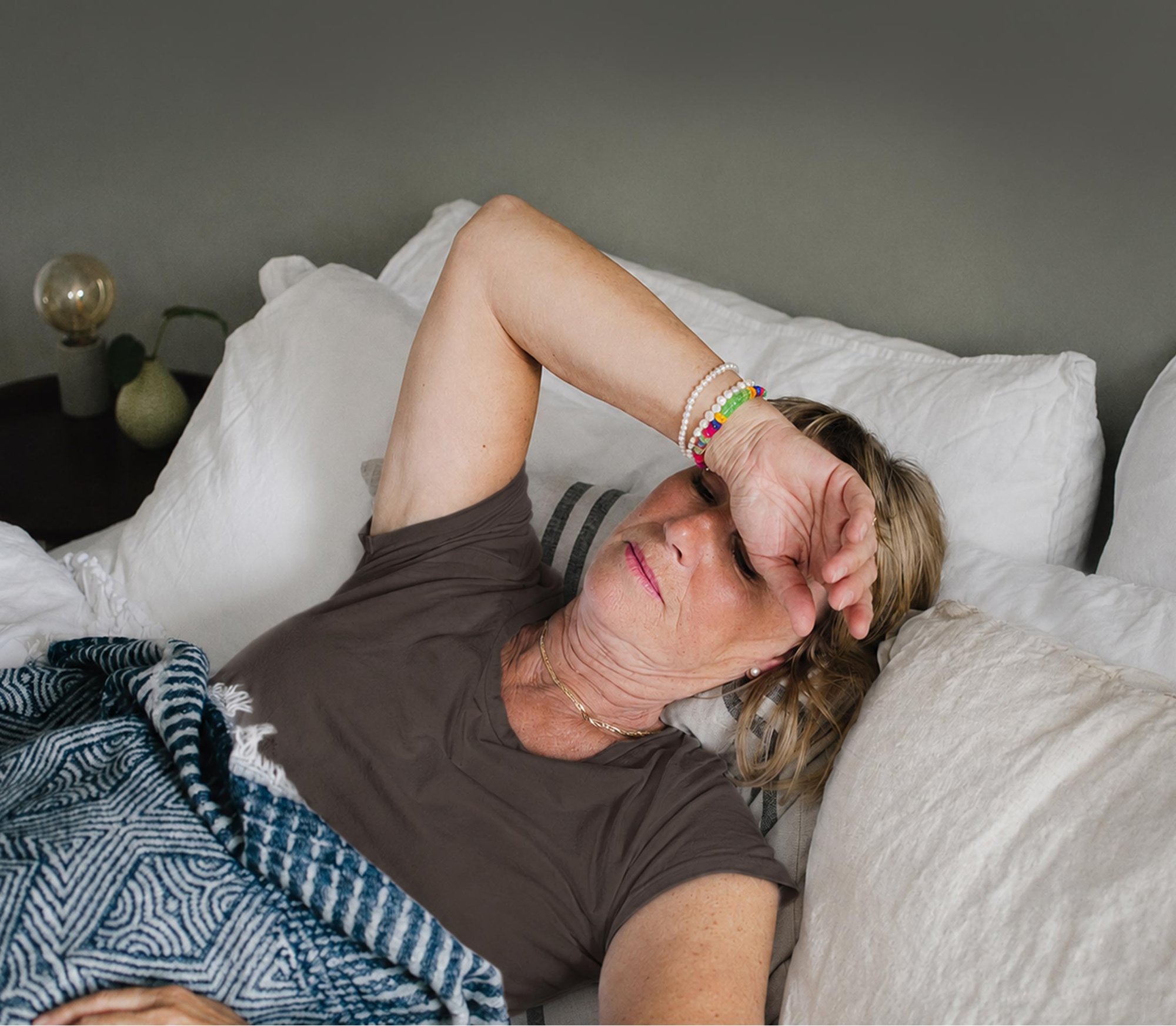 Kvinne hviler i sengen med hånden på pannen. Illustrasjonsfoto til artikkel om kvalme ved metastatisk brystkreft.