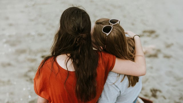 To tenåringer, jenter, bakfra på en strand. De holder rundt hverandre og søker trøst og støtte når mamma har brystkreft.