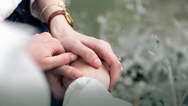 Nærbilde av to personers hender, som omsorgsfullt holder hverandre i hånden. Foto.