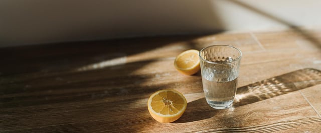Et glass vann og to halve sitroner på et trebord – enkle hjelpemidler mot kvalme ved kreftbehandling.