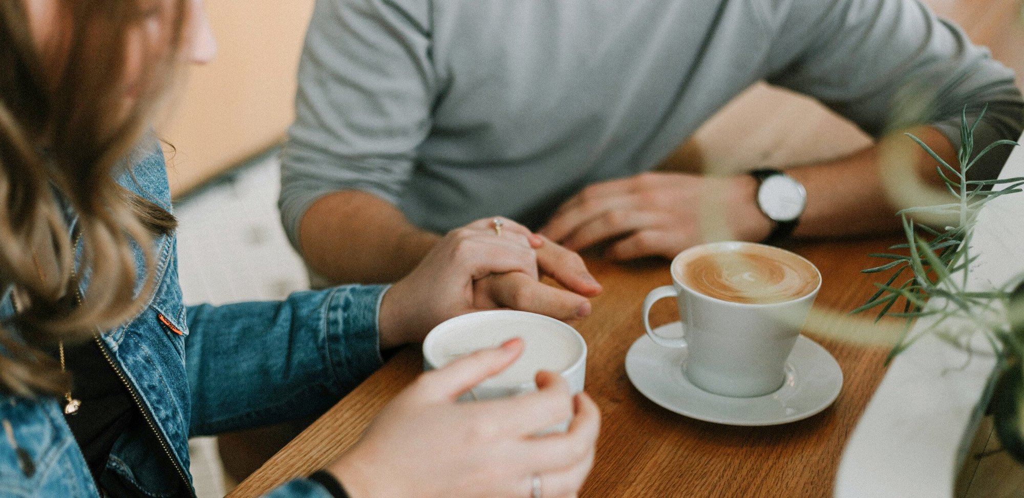 Nærbilde av to damer på kafé, den ene er likeperson og holder hånden støttende på den andre. De sitter med hver sin kaffekopp.