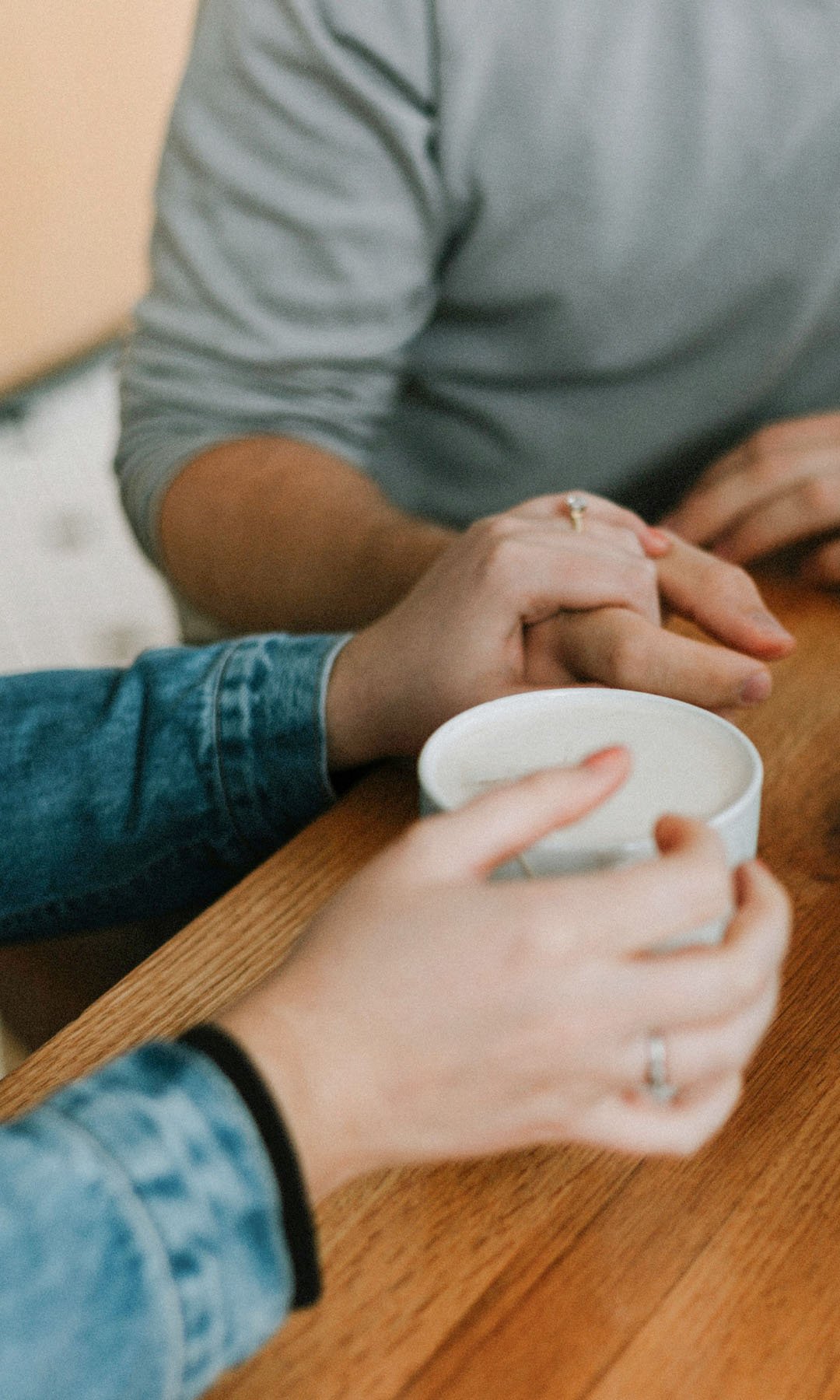 Nærbilde av to damer på kafé, den ene er likeperson og holder hånden støttende på den andre. De sitter med hver sin kaffekopp.