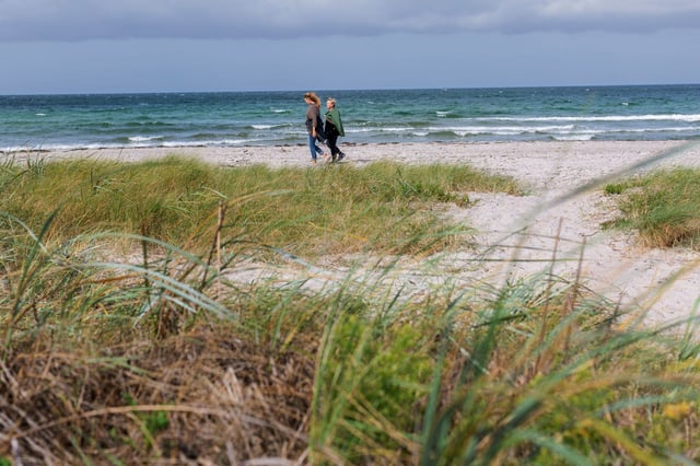 En eldre kvinne med brystkreft går langs stranden med sin yngre datter. Foto.