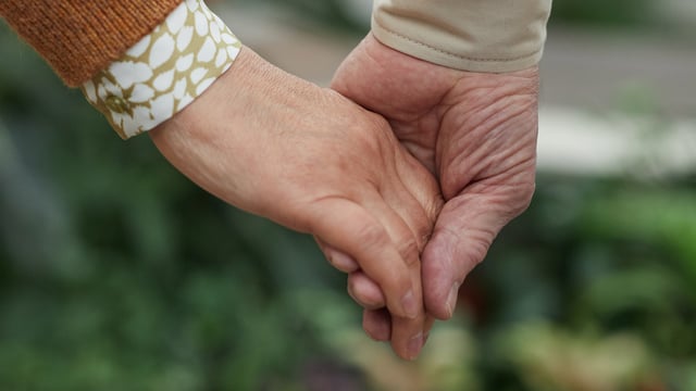 Nærbilde av to som kjemper mot kreft og holder hender. Illustrasjonsfoto