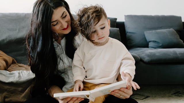 En mor med etnisk bakgrunn og brystkreft med spredning som leser en bok for sin sønn som sitter på fanget hennes. Illustrasjonsfoto