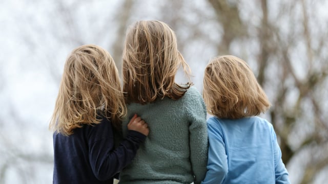 Tre barn som er pårørende til en med brystkreft stadium 4 står tett sammen ute i naturen på høsten med ryggen mot kameraet. Illustrasjonsfoto
