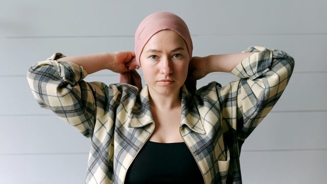 Kvinne som binder et sjal rundt hodet. Hun har ikke hår på grunn av brystkreft. Kvinnen ser direkte inn i kameraet. Illustrasjonsfoto