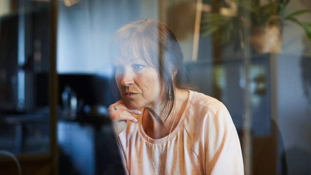 Kvinne med brystkreft med spredning som sitter ved en PC og jobber. Illustrasjonsfoto.