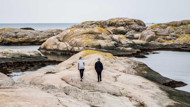 To personer går tur på svaberg ved havet. Illustrasjonsfoto