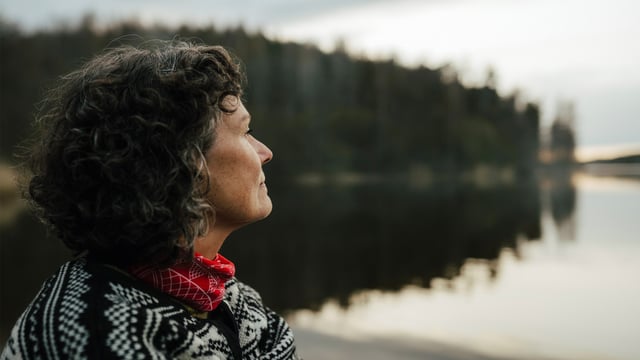 Kvinne med brystkreft med spredning som ser ut over stille vann. Illustrasjonsfoto
