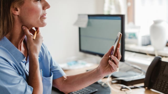 Kvinnelig kreftlege sitter på kontoret og ser på statistikk på sin mobiltelefon. Illustrasjonsfoto