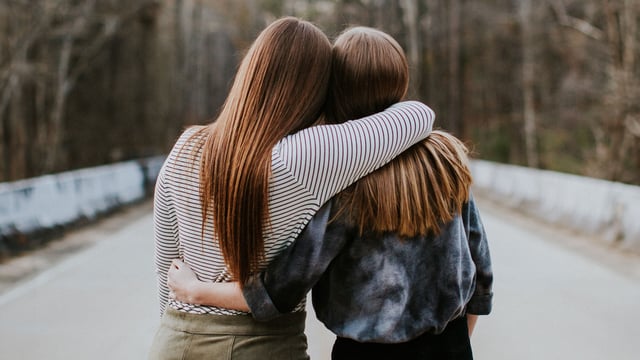 To venninner sett bakfra står side om side og holder rundt hverandre. Illustrasjonsfoto